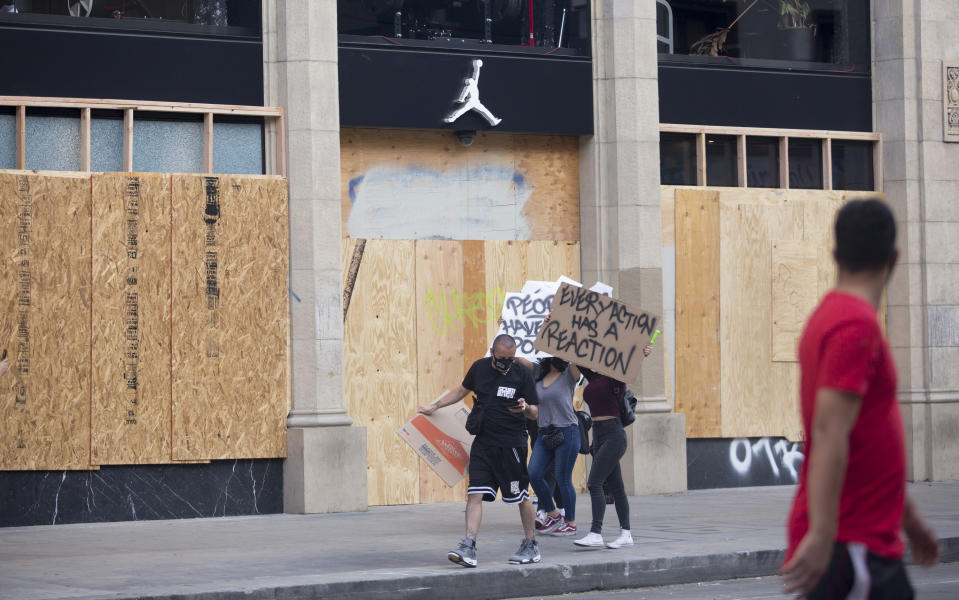 Protesters past by a NIKE store boarded up with a wood slabs as protests over the death of George Floyd continue Sunday, May 31, 2020, in Los Angeles. Armed National Guard soldiers lined the steps of Los Angeles City Hall, and cities across California declared curfews Sunday to head off more violence. (AP Photo/Ringo H.W. Chiu)