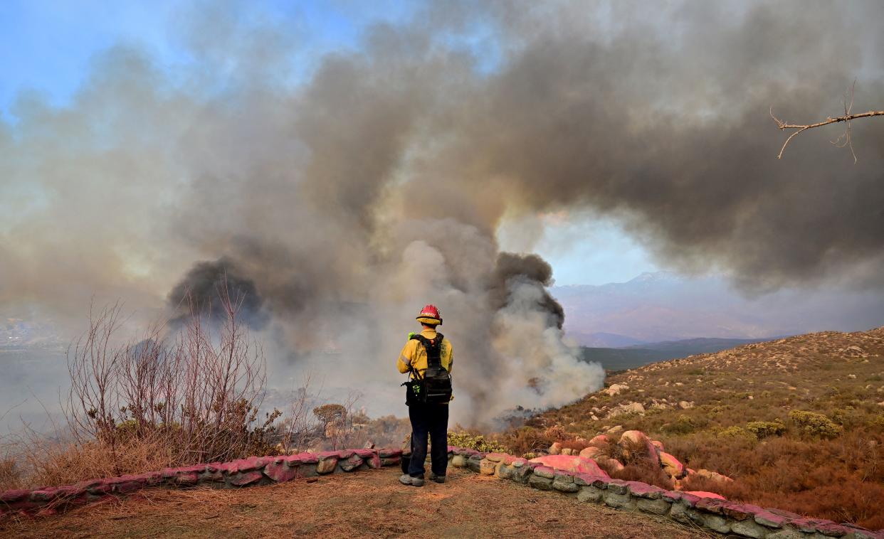 A firefighter is seen from behind as smoke erupts from a hillside fire.