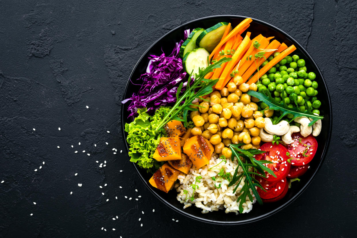 Bowl dish with brown rice, cucumber, tomato, green peas, red cabbage, chickpea, fresh lettuce salad and cashew nuts. Healthy balanced eating