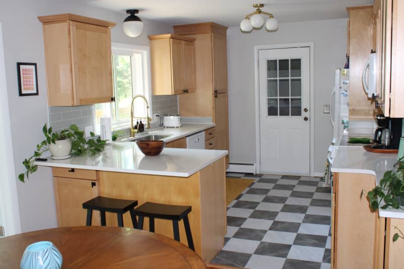 Light wood cabinets with white stone counter and checker flooded kitchen.