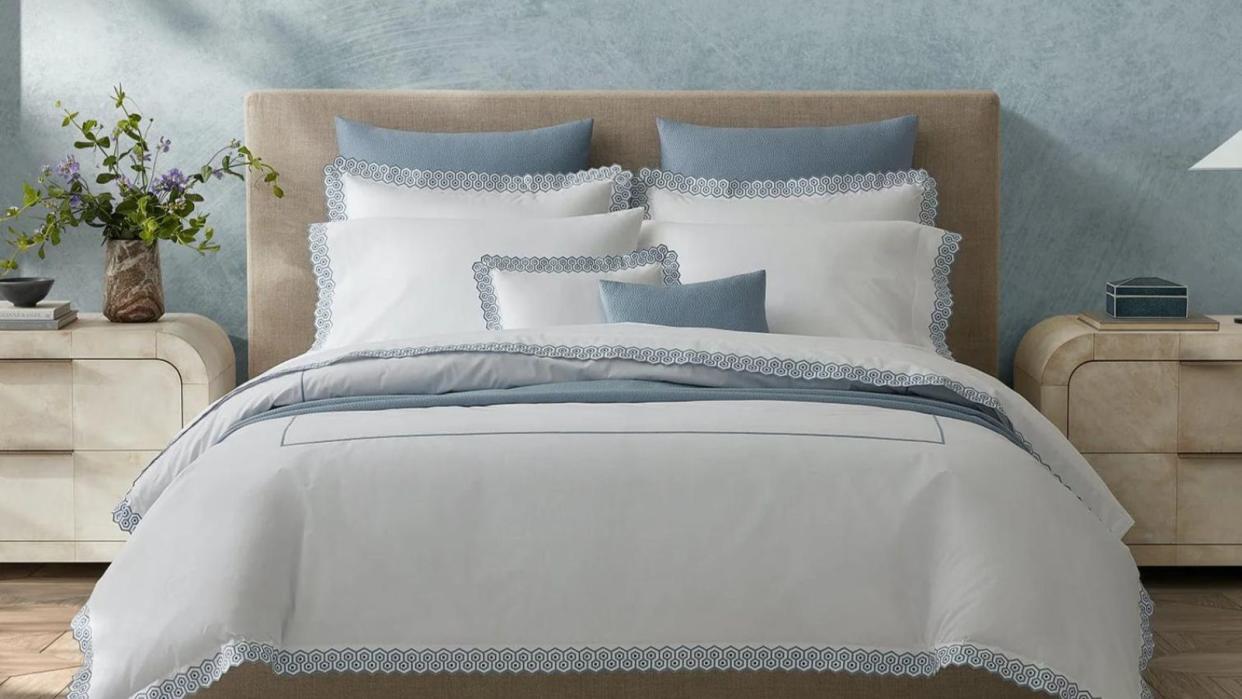  Some of the items in the luxury bedding sales - Matouk Felix Linens on a bed against a blue wall. 