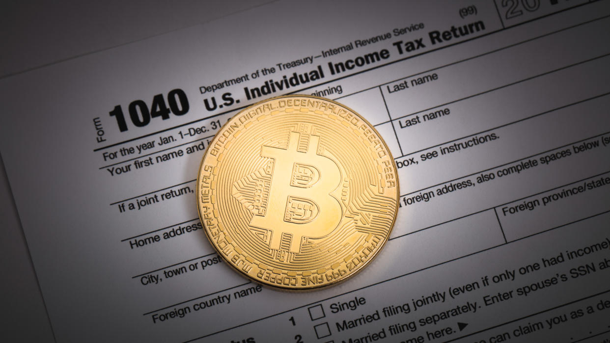 An editorial stock photo of a studio shot of a Bitcoin with some IRS 1040 tax forms.