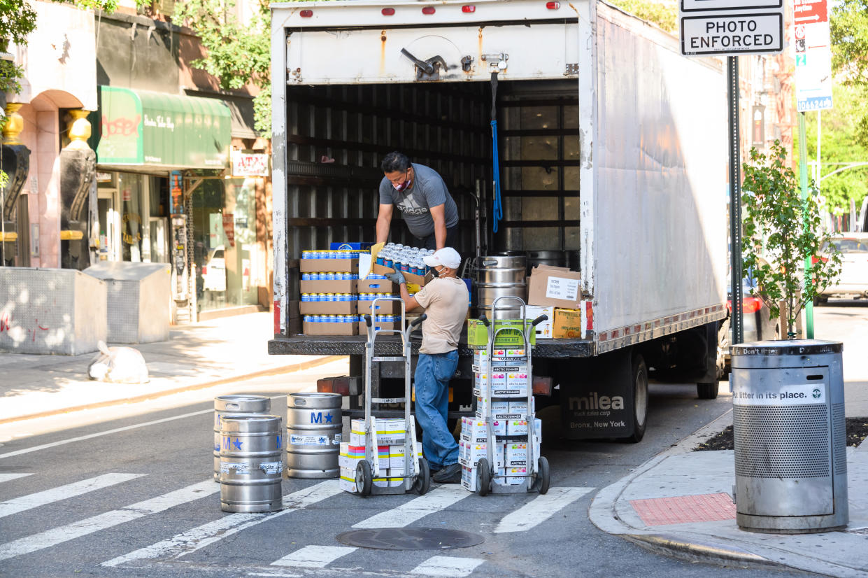 Two workers unload cases of beer from a truck.