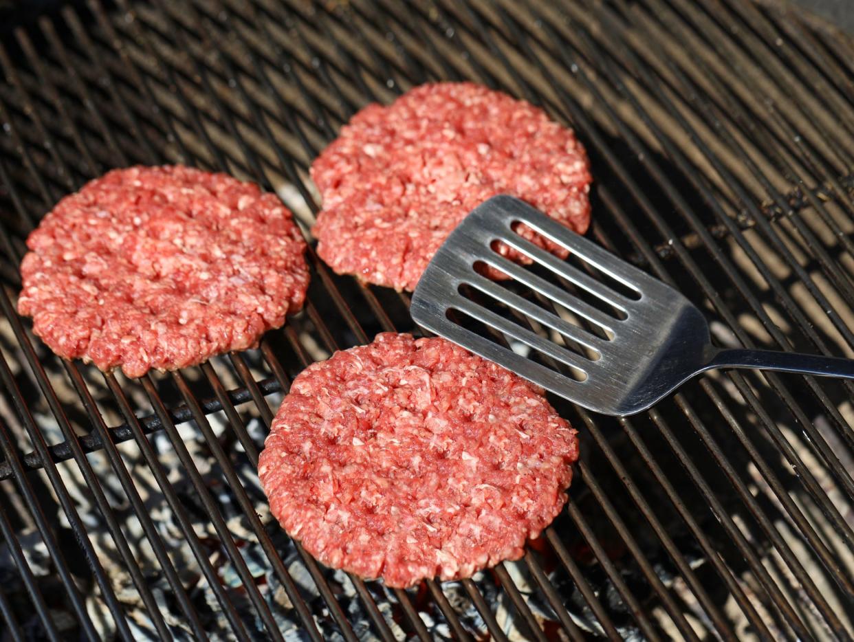 top view of raw beef hamburger patties on barbecue grill grate with spatula.