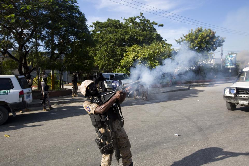 Police disperse the crowd with tear gas, away from the site where a car that careened out of control hit a group of persons in Port-au-Prince, Haiti, Wednesday, Nov. 21, 2018. According to the police the car, that was set alight by protesters, lost a wheel when it lost control and killed six persons on the street. The deaths come as Haiti faces a fourth day of protests to demand that President Jovenel Moise resign for not investigating allegations of corruption in the previous government over Petrocaribe, a Venezuelan subsidized energy program. (AP Photo/Dieu Nalio Chery)