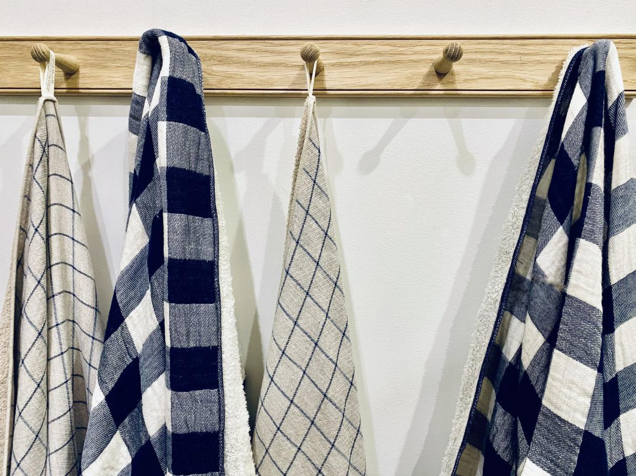 Horizontal close up of domestic kitchen white wall with wood hook rail rack holding cream and blue checkered tea towels and dish cloths