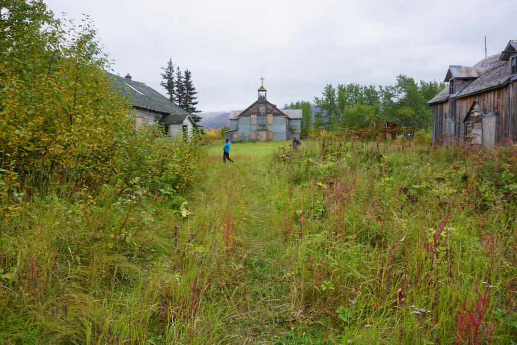 Visitors on Sept. 4, 2021, stroll by the historic chapel and buildings used for classrooms and dormitories that remain standing at Pilgrim Hot Springs, a site used as an orphanage for Bering Strait-area children who lost their parents to the 1918 influenza epidemic. (Photo by Yereth Rosen/Alaska Beacon)