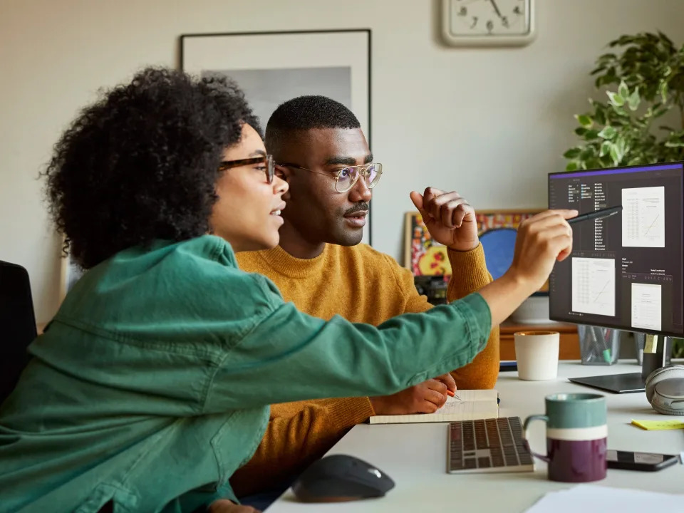 Businesswoman discussing with businessman over computer. Male and female entrepreneurs are working at a desk. They are sitting at a home office.