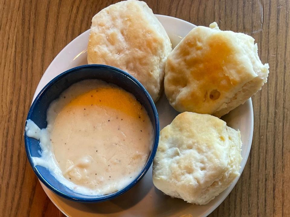 Three biscuits on a plate with a small bowl of gravy