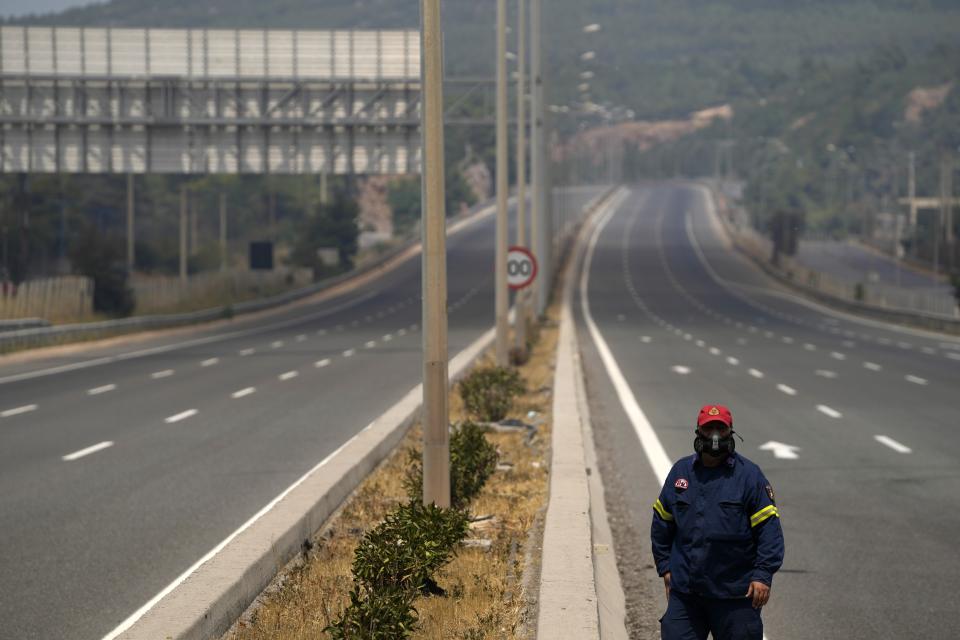 A firefighters walks on the closed highway at during a wildfire in Kapandriti village, about 38 kilometres (23 miles) north of Athens, Greece, Friday, Aug. 6, 2021. Thousands of people fled wildfires burning out of control in Greece and Turkey on Friday, as a protracted heat wave turned forests into tinderboxes and flames threatened populated areas, electricity installations and historic sites. (AP Photo/Thanassis Stavrakis)