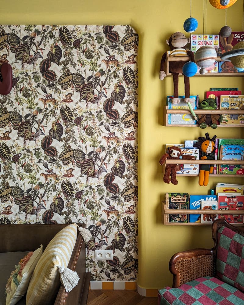 Yellow kids room with botanical wallpaper accent wall, brown leather and wood bed, and floating book/toy shelves