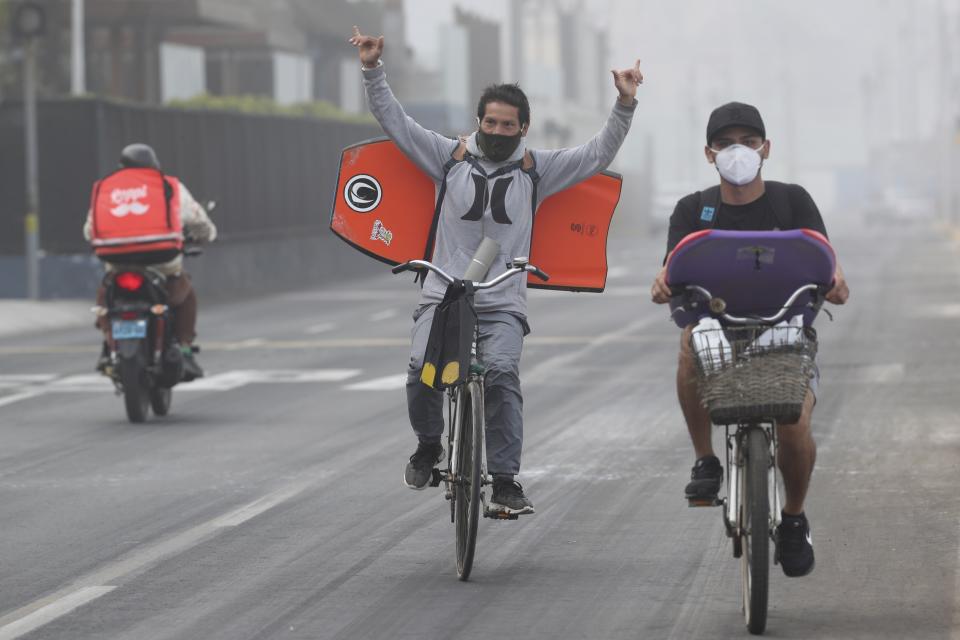 Wearing face masks as a precaution amid the spread of the new coronavirus, surfers cycle to Waikiki Beach in the Miraflores district of Lima, Peru, Thursday, June 11, 2020. The emblematic surfers who dot Peru's coastline are retaking to the waves as the hard-hit nation relaxes COVID-19 related restrictions on outdoor sports. (AP Photo/Martin Mejia)