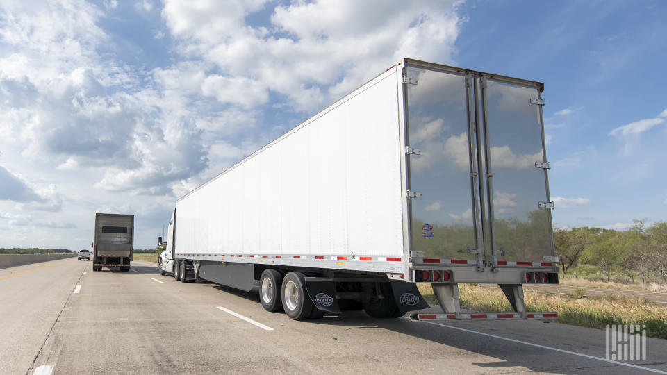 A white trailer being pulled by a white tractor on a highway