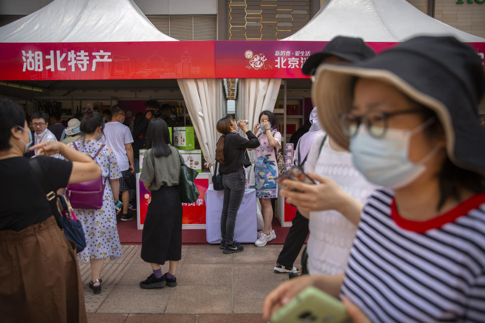 People wearing face masks to protect against the new coronavirus browse merchant tents at a government event aiming to stimulate consumer demand and consumption in Beijing, Saturday, June 6, 2020. China's capital is lowering its emergency response level to the second-lowest starting Saturday for the coronavirus pandemic. That will lift most restrictions on people traveling to Beijing from Wuhan and surrounding Hubei province, where the virus first appeared late last year. (AP Photo/Mark Schiefelbein)