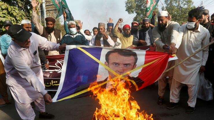 Demonstranten in Pakistan verbrennen eine Fahne mit einem Bild des französischen Präsidenten Macron darauf. Der Karikaturenstreit gilt als Auslöser der jüngsten Proteste – doch dass Frankreich in der muslimischen Welt wiederholt zur Zielscheibe wird, hat auch andere Ursachen. Foto: dpa