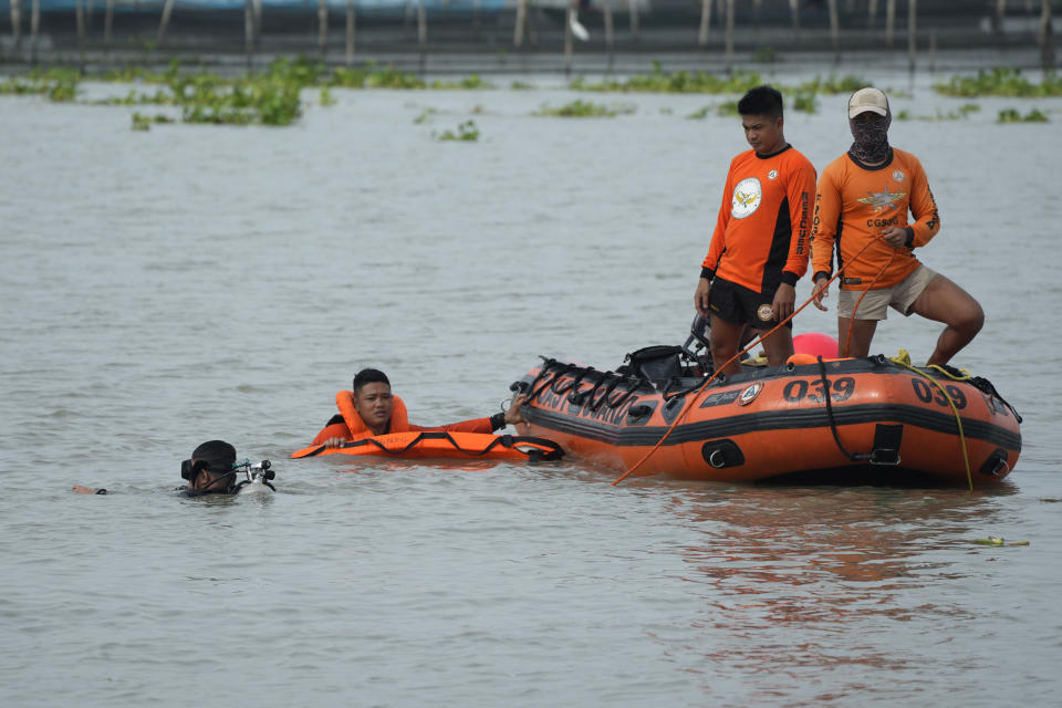 Rescuers search for victims of a capsized ferry as a passenger boat cruises nearby in Binangonan, Rizal province, Philippines, Friday, July 28, 2023. A boat turned upside down on Thursday when passengers suddenly crowded to one side in panic as fierce winds pummeled the wooden vessel, killing a number of people, officials said Friday. (AP Photo/Aaron Favila)