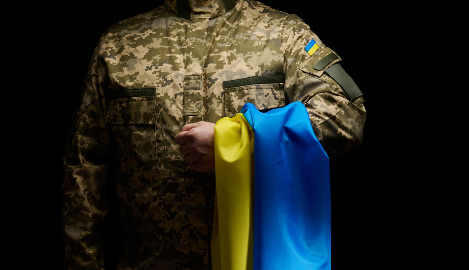 a soldier of the Ukrainian armed forces stands with a blue-yellow flag of Ukraine on a black background. Honoring veterans and commemorating those killed in the war