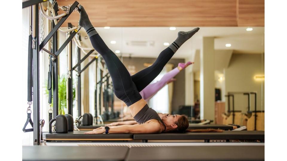 Sportspeople doing short spine pilates exercises on a reformer bed in a gym during a workout to align and balance her core muscles in a health and fitness concept.