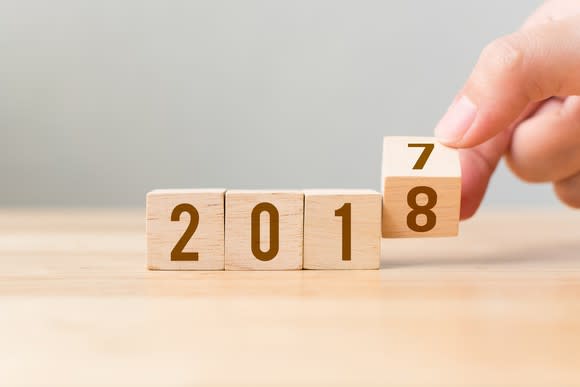 A hand flips a wooden cube indicating the transition to 2018.