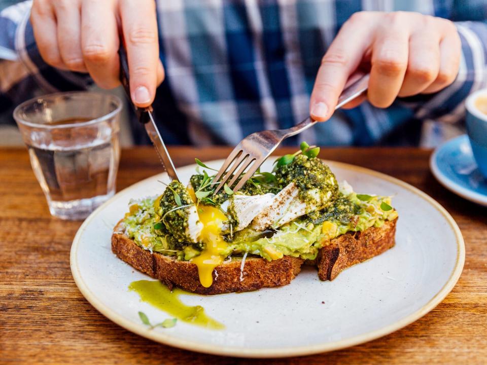 a person cutting avocado toast with egg with a fork and knife
