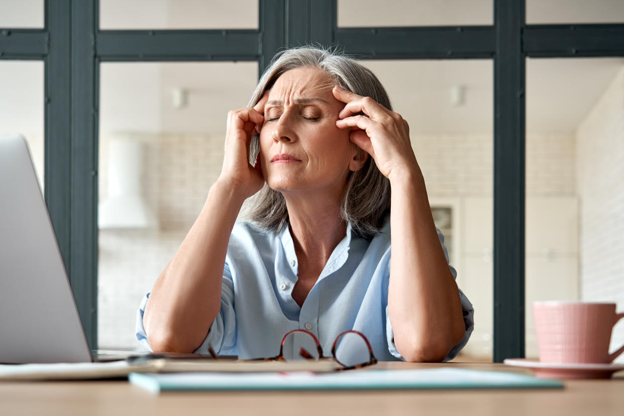 Tired stressed old mature business woman suffering from headache at work. Upset sick senior middle aged lady massaging head feeling migraine from overwork or menopause using computer at home office.