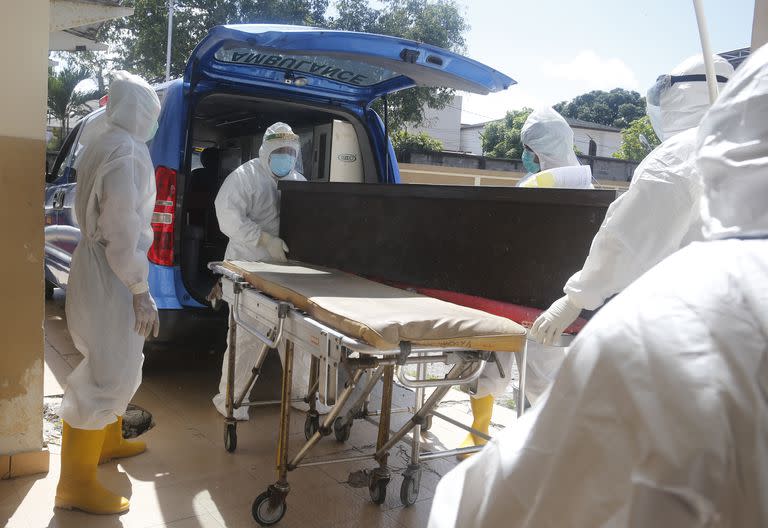 Trabajadores de la salud, equipados con trajes de protección, meten el féretro de una persona fallecida por COVID-19 en una ambulancia antes de enterrarlo, Denpasar, Bali, Indonesia.