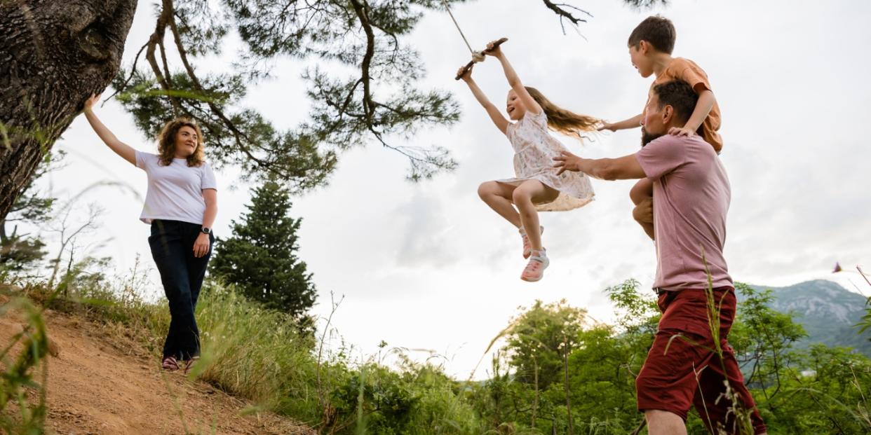 Mother And Father Play With Siblings On The Tree Swing