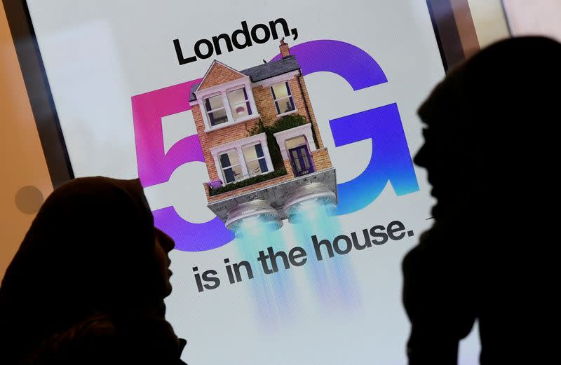 FILE PHOTO: Pedestrians walk past an advertisement promoting the 5G data network at a mobile phone store in London