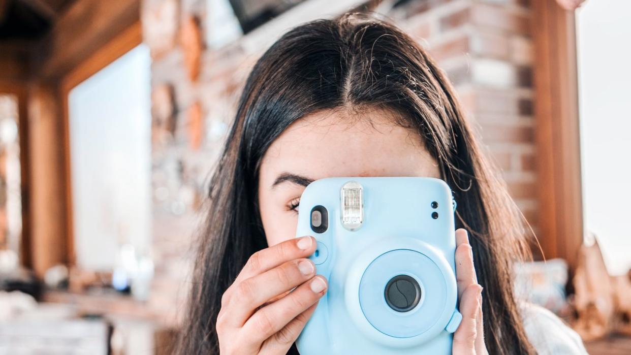 adolescent girl using a blue instant camera