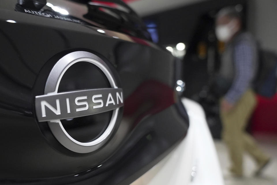 A visitor walks near a Nissan logo attached to a car at Nissan headquarters Thursday, May 12, 2022, in Yokohama near Tokyo. Japanese automaker Nissan returned to profitability in the last fiscal year for the first time in three years, despite challenges such as supply shortages caused by the pandemic and soaring costs. (AP Photo/Eugene Hoshiko)