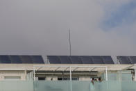 A couple stand in their balcony, with solar panels are on the roof of the building in Rivas Vaciamadrid, Spain, Thursday, Sept. 15, 2022. The energy crisis is accelerating the installation of solar panels by residential communities in Spain who want to become self-sufficient. Recent legislation has allowed so-called "energy communities" to generate renewable power through collective installations. (AP Photo/Manu Fernandez)