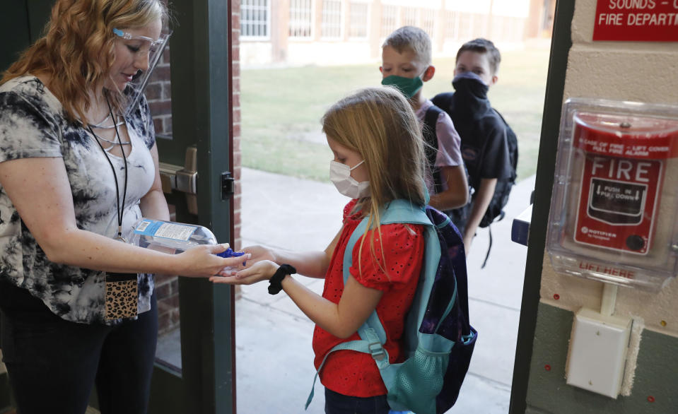 FILE - In this Aug. 5, 2020, file photo, wearing masks to prevent the spread of COVID19, elementary school students use hand sanitizer before entering school for classes in Godley, Texas. As schools reopen around the country, their ability to quickly identify and contain coronavirus outbreaks before they get out of hand is about to be put to the test. (AP Photo/LM Otero, File)