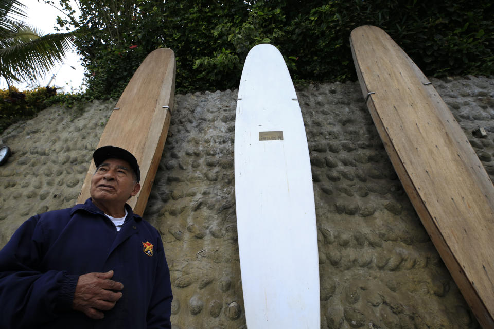 In this July 26, 2019 photo, Victor "Mamico" Curo, 79, who has cared for surfboards at Club Waikiki for 60 years, stands in front of a trio of historic surfboards, including one marked with a plaque saying it was given to club founder Carlos Dogny in the 1930s by Hawaiian surfer Duke Kahanamoku, at the beachfront surf club in Lima, Peru. Surfing is a way of life in Peru, which has been called the Hawaii of Latin America. (AP Photo/Rebecca Blackwell)