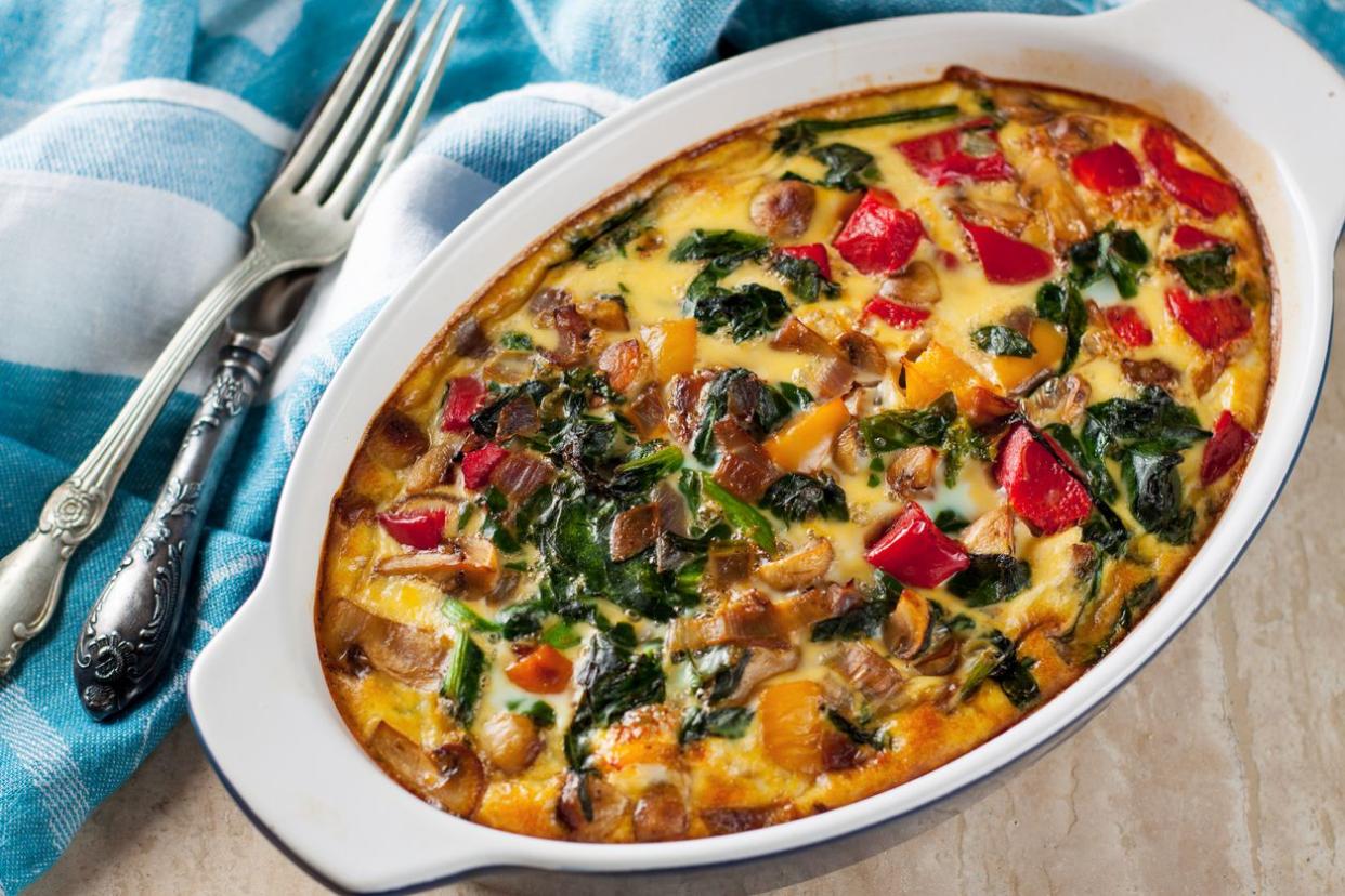 Casserole with tomatoes, mushrooms and spinach in oval white and black individual portion baking dish with a blue and white checkered cloth napkin