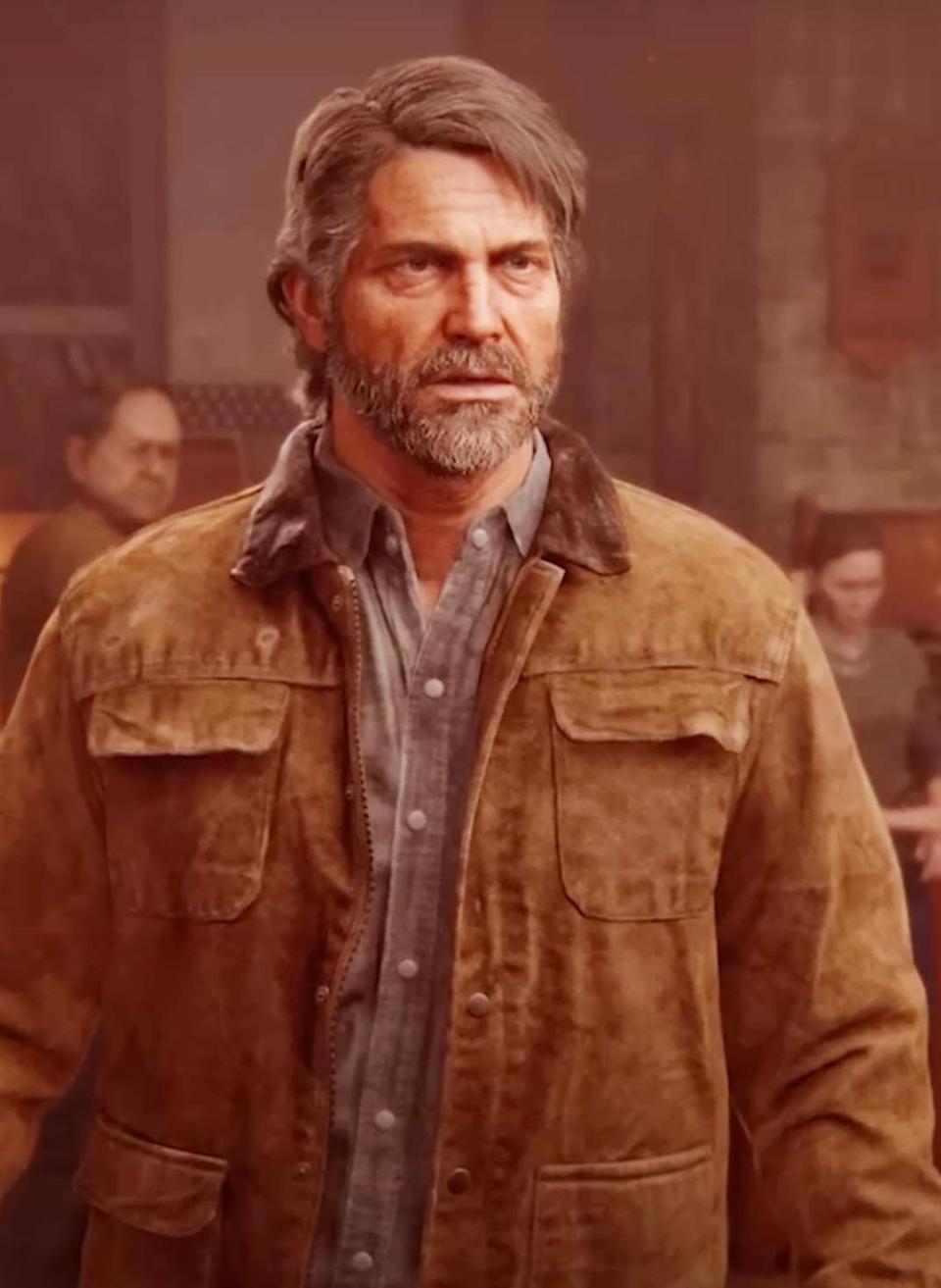 Joel from The Last of Us Part II video game, with a beard and a brown jacket, stands in a dimly lit room