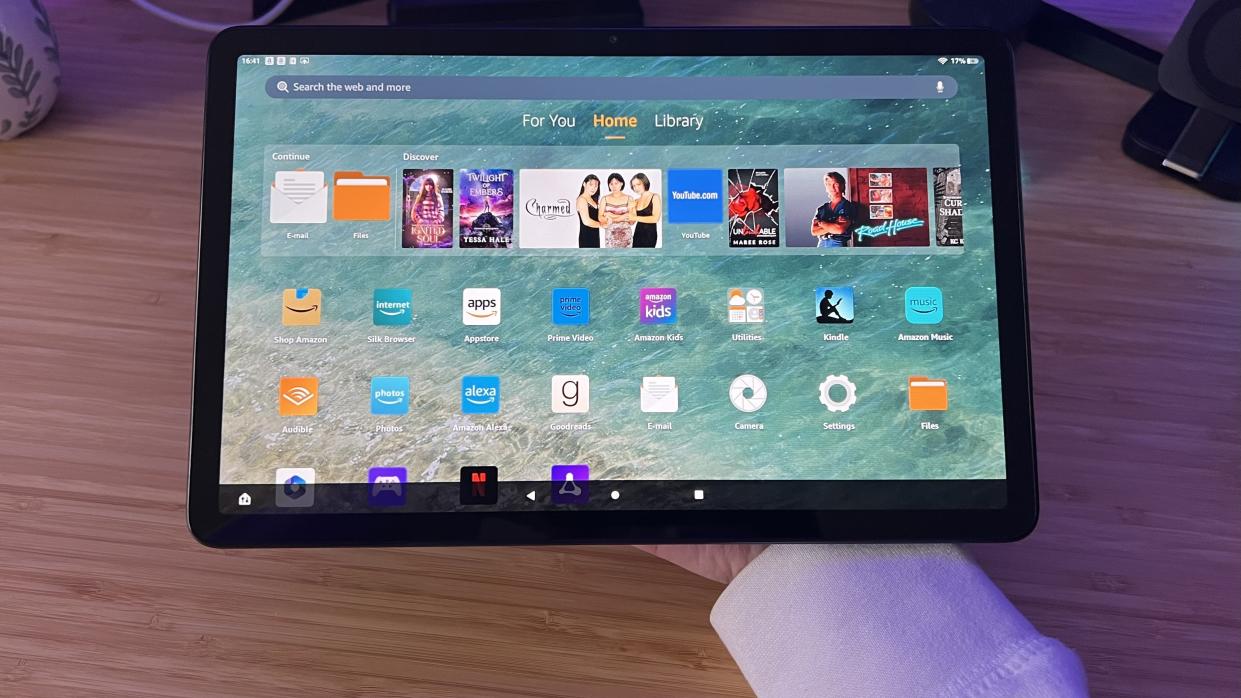  Amazon Fire Max 11 being held along the back panel over a wooden desk. 
