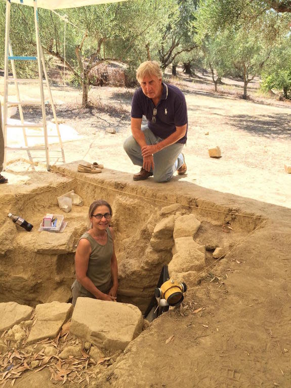 Sharon Stocker stands in the shaft tomb the team uncovered. Jack Davis kneels beside the tomb.