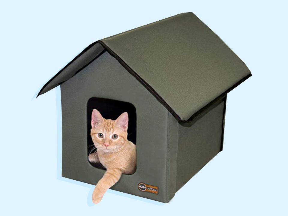 A green K&H Pet Products Outdoor Heated Kitty House with orange cat lying inside.