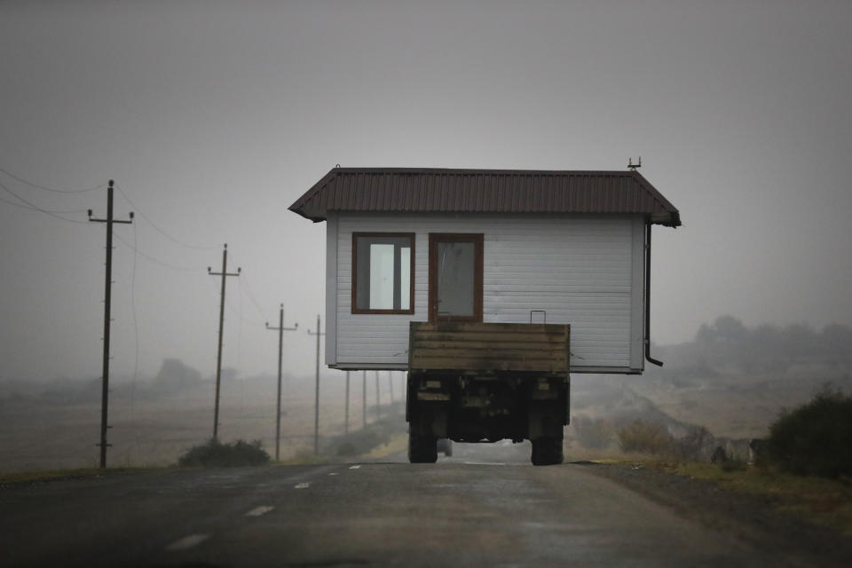 A family drives a truck loaded with a small house along a highway as they leave their home village in the separatist region of Nagorno-Karabakh, Wednesday, Nov. 18, 2020. A Russia-brokered cease-fire to halt six weeks of fighting over Nagorno-Karabakh stipulated that Armenia turn over control of some areas it holds outside the separatist territory's borders to Azerbaijan. Armenians are forced to leave their homes before the region is handed over to control by Azerbaijani forces. (AP Photo/Sergei Grits)