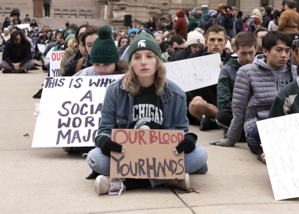 Protesters sit on the ground holding signs.