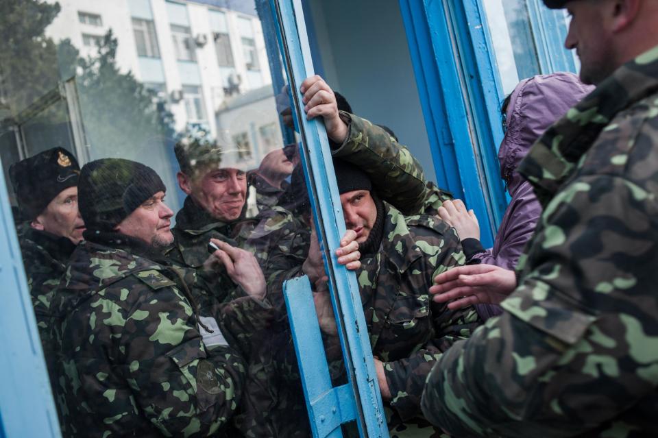 Pro-Russian self-defense force members get through an entrance to the Ukrainian Navy headquarters in Sevastopol, Crimea, Wednesday, March 19, 2014. An Associated Press photographer said several hundred militiamen took down the gate and made their way onto the base. They then raised the Russian flag in the square by the headquarters. The unarmed militia waited for an hour on the square before the move to storm the headquarters. Following the arrival of the commander of the Russian Black Sea fleet, the Crimeans took over the building. (AP Photo/Andrew Lubimov)