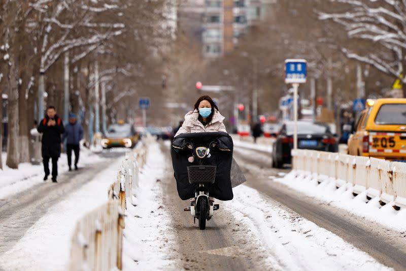 Una mujer conduce una moto por una carretera tras una nevada en Pekín