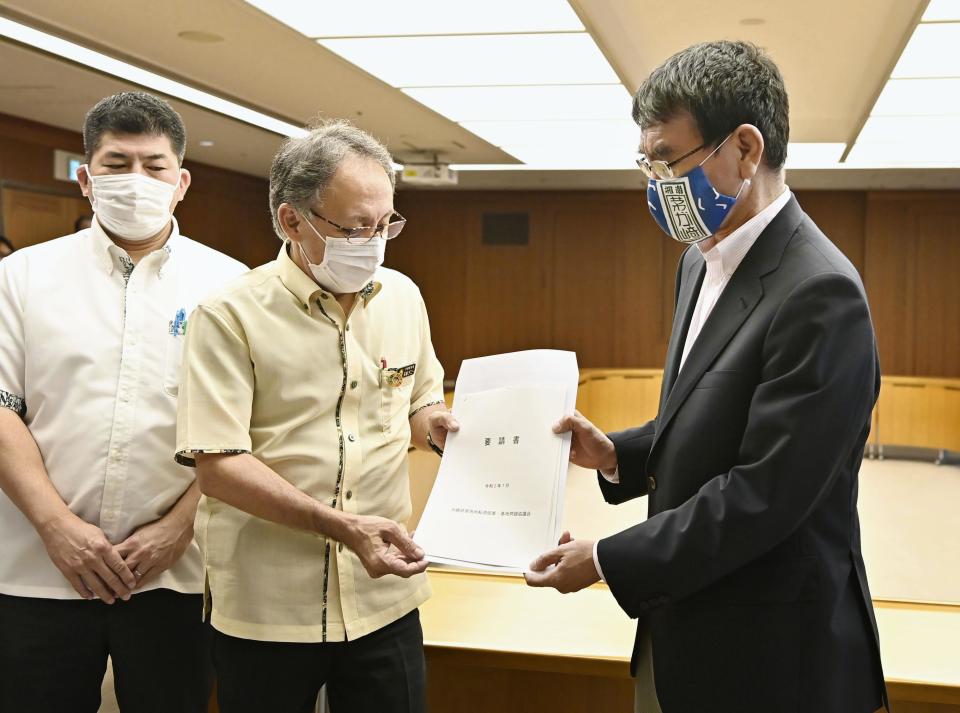 Okinawa Gov. Denny Tamaki, center, and Japanese Defense Minister Taro Kono, right, hold Okinawa's request document during their meeting at the Defense Ministry in Tokyo, Wednesday, July 15, 2020. Gov. Tamaki urged Japan's government to pressure the U.S. military to better guard against an escalating coronavirus outbreak that has infected more than 130 Marines stationed on the southern Japanese island, triggering fear of infections spreading outside of the bases.(Ren Onuma/Kyodo News via AP)