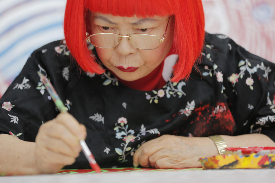 In this photo taken Wednesday, Aug. 1, 2012, Japanese avant-garde artist Yayoi Kusama, wearing a bright red wig, works at her studio in Tokyo. Kusama's signature splash of dots has now arrived in the realm of fashion in a new collection from French luxury brand Louis Vuitton - bags, sunglasses, shoes and coats. The latest Kusama collection is showcased at its boutiques around the world, including New York, Paris, Tokyo and Singapore, sometimes with replica dolls of Kusama. (AP Photo/Itsuo Inouye)