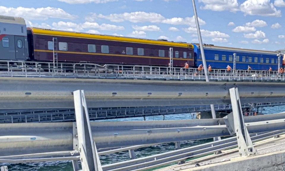 In this image from a video released on Wednesday, July 19, 2023 by the Russian National Antiterrorism Committee, A passenger train passes by the damaged parts of an automobile link of the Crimean Bridge connecting Russian mainland and Crimean peninsula over the Kerch Strait not far from Kerch, Crimea. (Russian National Antiterrorism Committee via AP)