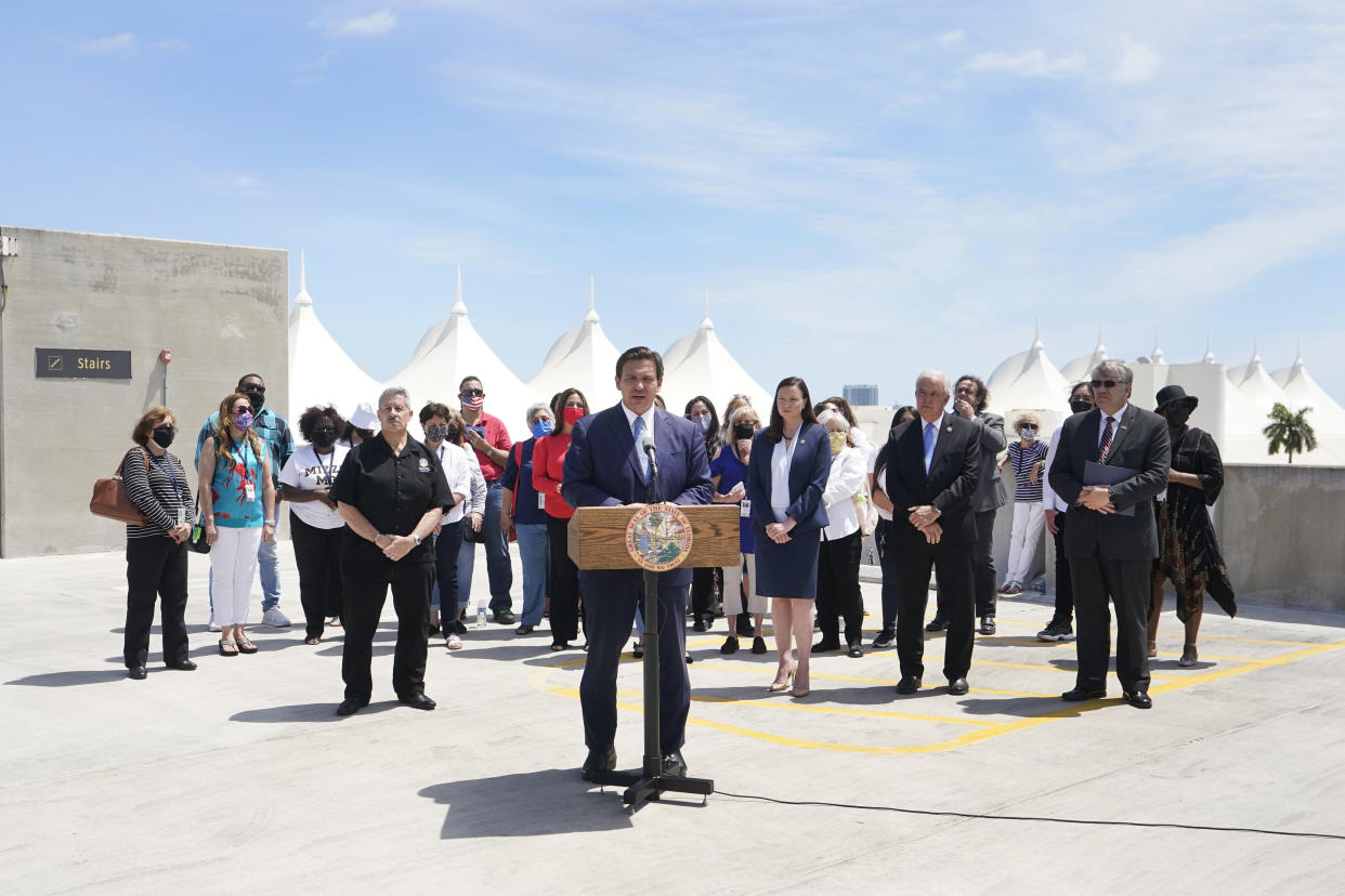 Florida Gov. Ron DeSantis, center, speaks during a news conference surrounded by cruise workers, Thursday, April 8, 2021, at PortMiami in Miami. DeSantis announced a lawsuit against the federal government and the CDC demanding that cruise ships be allowed to sail. (AP Photo/Wilfredo Lee)
