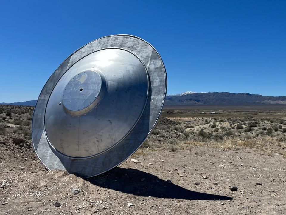 A silver flying saucer standing up in the dessert ground.
