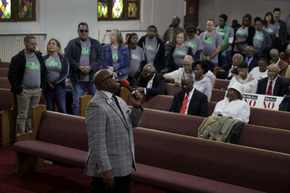 In this Sunday, Nov. 3, 2019, photo, people wearing "Save The Paseo" shirts stand among attendees at a rally to keep a street named in honor of Dr. Martin Luther King Jr. while Rev. Vernon Howard speaks at Paseo Baptist Church in Kansas City, Mo. In January, the City Council voted to rename one of the city's main boulevards, The Paseo, after King, but many in the community want the old name back. A petition drive put the issue on the Nov. 5 ballot pitting neighbors against each other. Ministers who pushed for the change worry about the message that will be sent if King's name is removed. (AP Photo/Charlie Riedel)