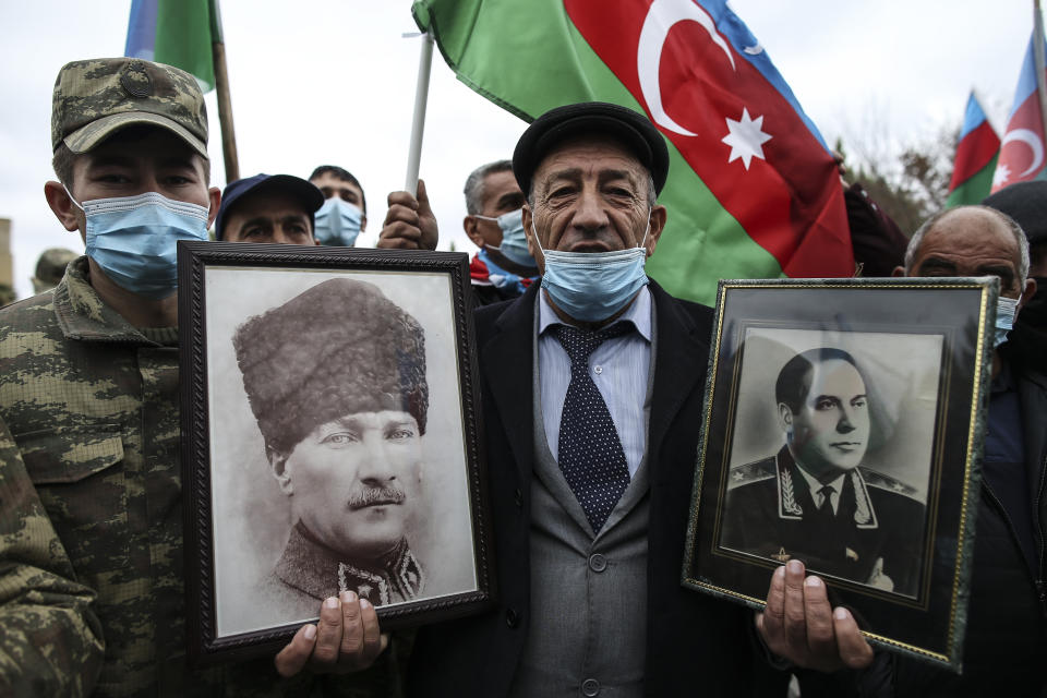 CORRECTING IDENTY OF PORTRAITS TO TURKEY’S FOUNDER MUSTAFA KEMAL ATATURK, LEFT, AND AZERBAIJAN’S LATE PRESIDENT HAYDAR ALIYEV, RIGHT - An Azerbaijani man holds portraits of Turkey’s founder Mustafa Kemal Ataturk, left, and Azerbaijan’s late president Haydar Aliyev, father of Ilham Aliyev wearing in KGB Gen. Major uniform on the right, as he celebrates the transfer of the Lachin region to Azerbaijan's control, as part of a peace deal that required Armenian forces to cede the Azerbaijani territories they held outside Nagorno-Karabakh, in Aghjabadi, Azerbaijan, Tuesday, Dec. 1, 2020. Azerbaijan has completed the return of territory ceded by Armenia under a Russia-brokered peace deal that ended six weeks of fierce fighting over Nagorno-Karabakh. Azerbaijani President Ilham Aliyev hailed the restoration of control over the Lachin region and other territories as a historic achievement. (AP Photo/Emrah Gurel)