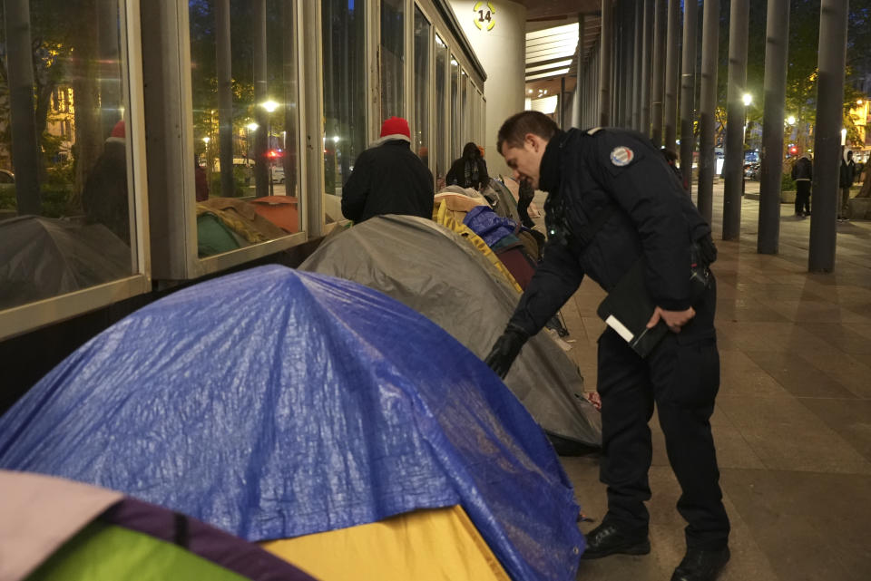 A police officers checks a migrant's tent in a makeshift camp, early Tuesday, April 23, 2024 in Paris. French police officers have evicted migrants from a makeshift camp in Paris a few steps away from the Seine River, as similar operations have been carried out by authorities ahead of the Olympics. (AP Photo/Nicolas Garriga)